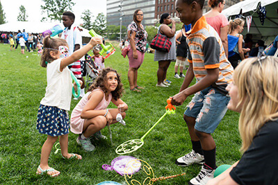 Diverse parents and children on a grassy area blowing bubbles